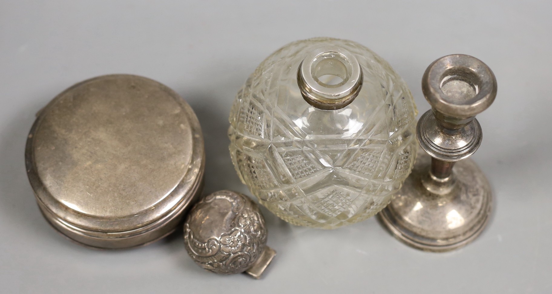 An Edwardian repousse silver mounted cut glass scent bottle(a.f.), a silver trinket box (no interior) and a silver mounted dwarf candlestick.